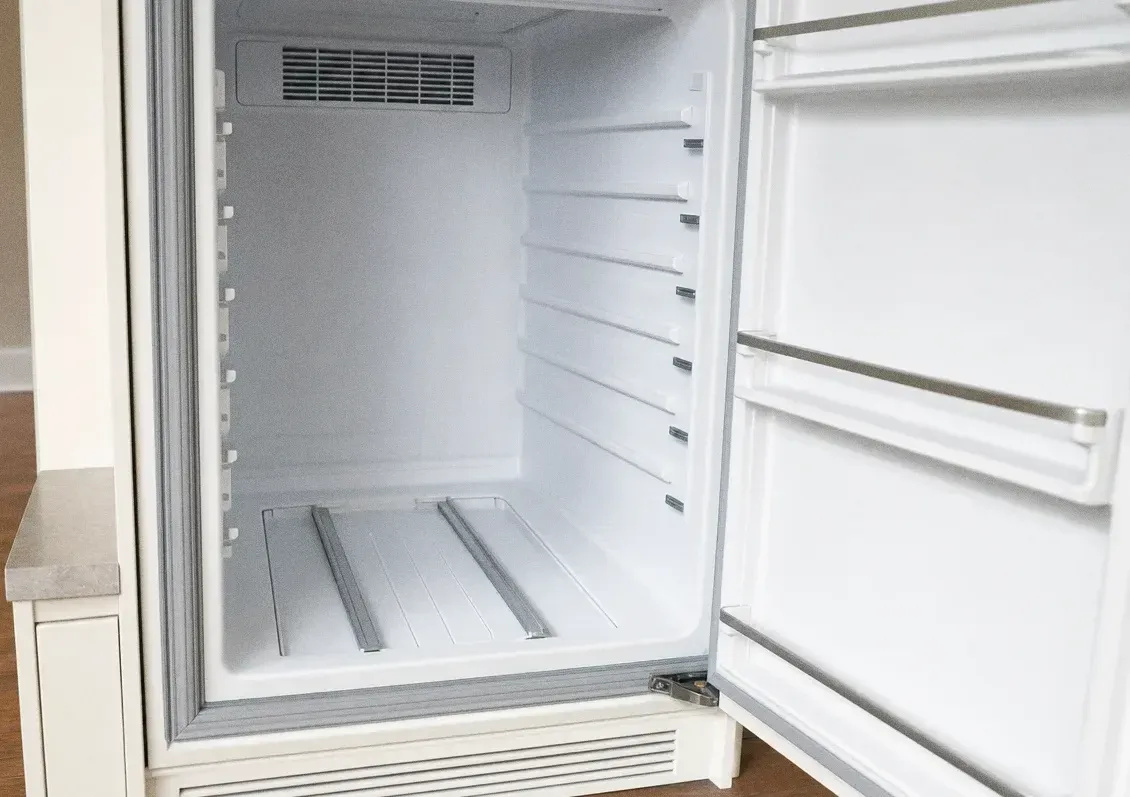 Empty white refrigeration cabinet with the door standing open and bare shelf rails inside
