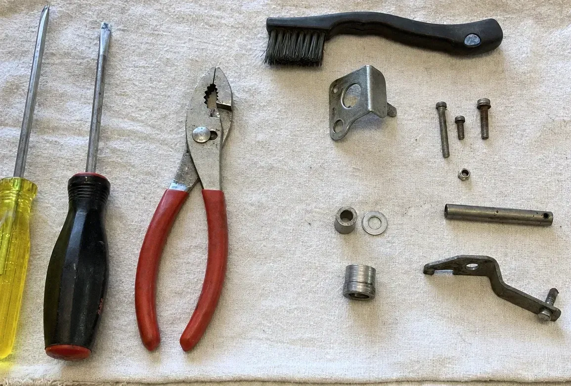 Screwdrivers, slip-joint pliers, a bracket, bolts and a bushing arranged on a canvas cloth